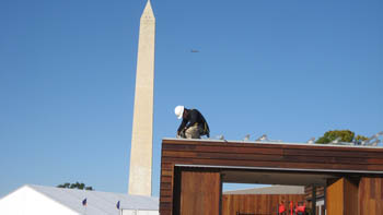 Photo of a man in a hard hat on the roof of a house with the Washington Monument just behind.
