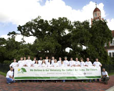 Photo 22 members of the Univ. of Louisiana team wearing white t-shirts and flanking a wide banner that reads: "We believe in our university, our culture, our state, our future. BeauSoleil Louisiana Solar Home."
