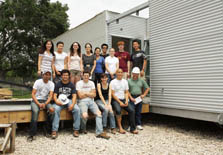 Photo of 15 members of the Rice University team on a deck extending from their unfinished Solar Decathlon house. The house is sided in corrugated metal.