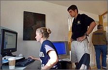 Photo of two students inside their solar house during the 2002 Solar Decathlon. One student is seated working on a computer and the second is standing looking at the computer monitor.