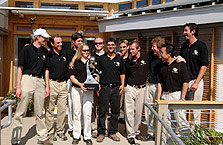 Photo of team members holding trophy standing on the porch of their house.