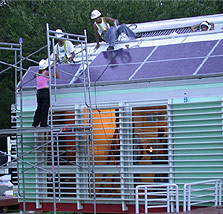 Photo of students installing solar electric panels on the roof of their house.