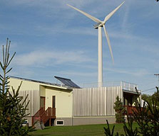 Photo of the Rhode Island School of Design solar-powered house with Portsmouth Abbey's wind turbine in the background.
