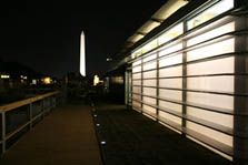 Photo of the glowing translucent walls of the Georgia Tech house with the Washington Monument lit up in the background.