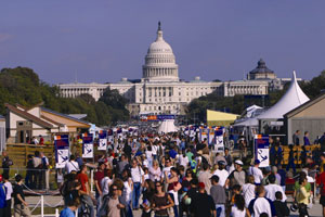 A photo of hundreds of people walking up the 2007 Solar Decathlon main street, which is surrounded by the homes built by the student teams.  The U.S. Capitol Building appears in the background framed by a clear blue sky.