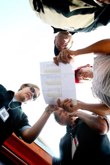 Photo that gives a view from the ground looking up at four people standing in a circle collectively holding and looking at a piece of paper