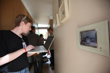 Photo of a man standing in a hallway and working on a laptop. In front of him is a digital display of the house's energy performance.