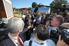Photo of Secretary Chu surrounded by people holding cameras and microphones. He is standing in front of the Team California house.