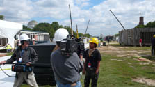 Photo of a three-person camera crew interviewing a student. In the background, cranes, unfinished houses, and the Capitol Building can be seen.