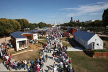 Photo of the Solar Decathlon solar village looking down Decathlete Way toward the Capitol Building. The walkway is crowded with people, who also form lines off to the sides toward the houses.
