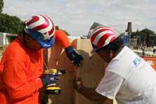 Photo of two men wearing hard hats and drilling a screw to secure a board to a short staircase.