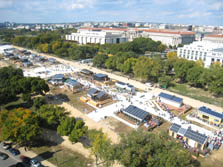 Aerial photo of the Solar Decathlon solar village that shows the houses lining Decathlete Way, which is filled with visitors. In the distance, numerous Washington, D.C., buildings are visible.