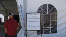 Photo of the entry to the Solar Decathlon workshop tent. A sign lists the day’s workshop schedule, and a visitor looks inside.